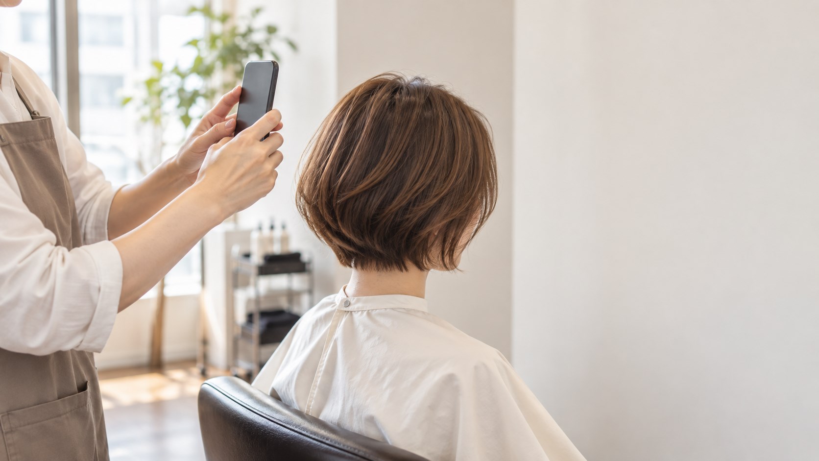 仕上がったショートヘアを、美容師がスマートフォンで後ろから撮影している